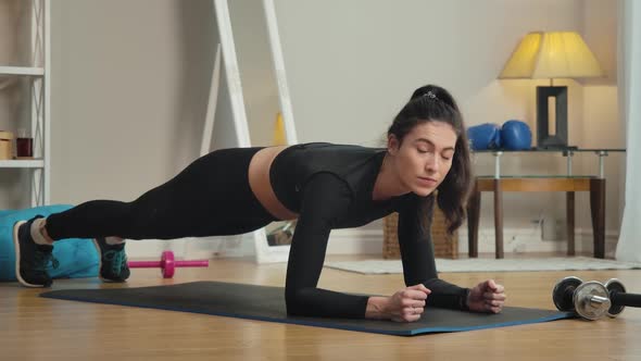 Concentrated Slim Woman Standing in Plank Position, Looking at Camera and Smiling. Portrait of