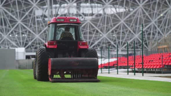 Back View of Worker on a Red Lawn Mower Pierces the Lawn Grass in a Football Stadium