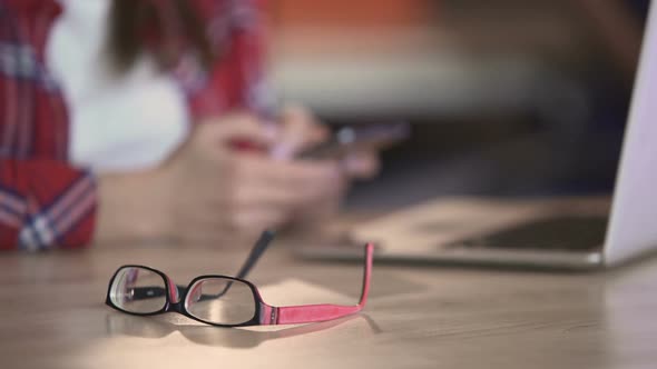 Stylish Eyeglasses Lying on Table, Woman Texting on Smartphone, Communication