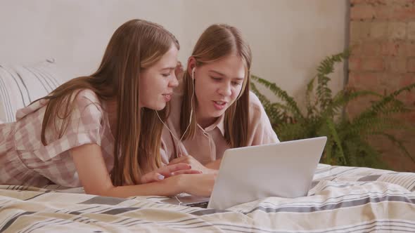 Twin Sisters in Earphones Using Laptop at Home