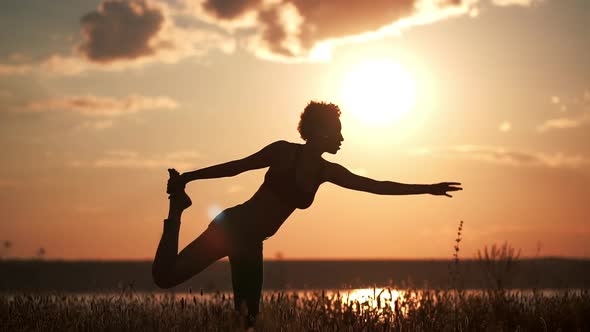 Silhouette of Young Beautiful Girl Practicing Yoga at Sunset