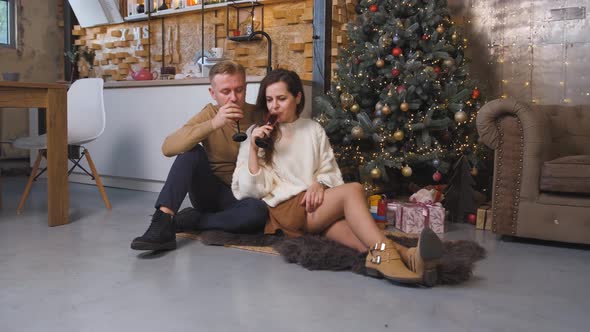 Young Couple Drinking Champagne While Sitting and Hugging Near the Christmas Tree
