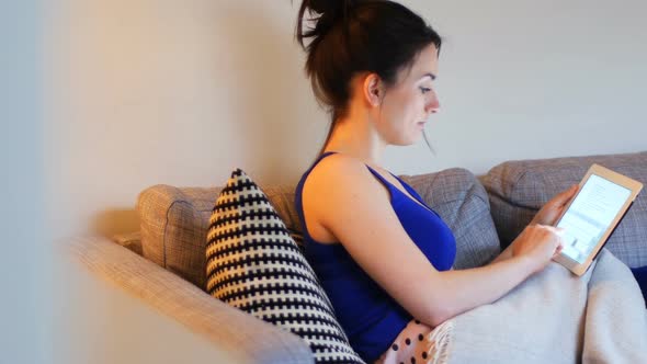 Woman using digital tablet on sofa in living room