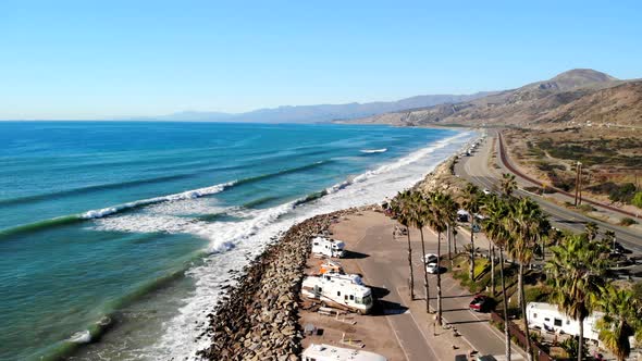 Aerial drone shot of a California beach paradise with blue ocean waves crashing against a palm tree