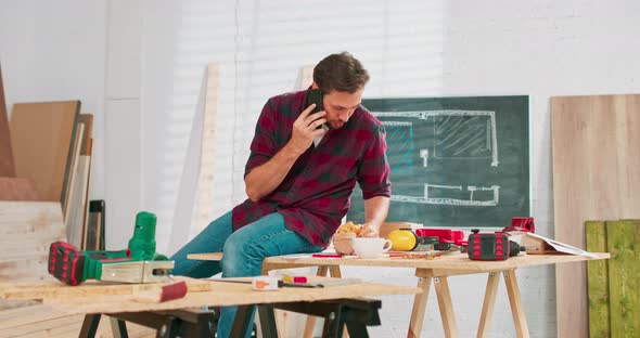 A Carpenter Uses a Smartphone During a Break at Work Young Handsome Craftsman is Resting in a