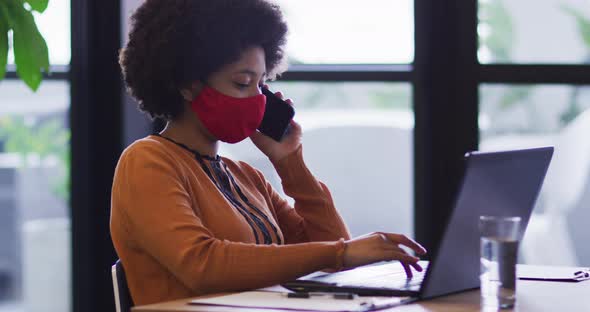 Mixed race businesswoman wearing mask sitting using a laptop in office