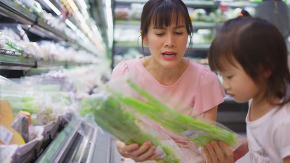 Asian young beautiful mother choosing grocery foods with little kid child walking in supermarket.