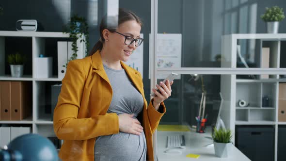 Cheerful Expecting Mother Office Worker Using Smart Phone Touching Screen in Workplace