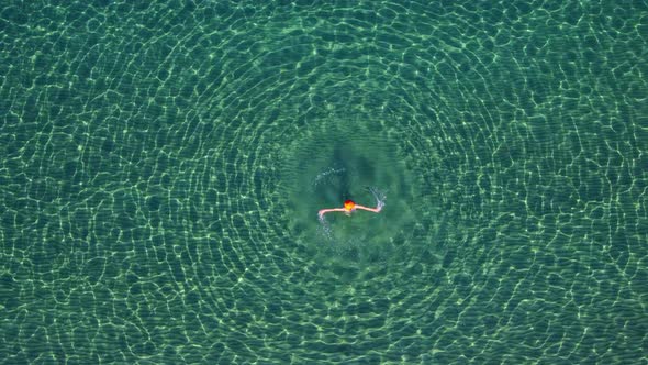 Aerial View a Woman in an Open Clear Transparent Sea is Spinning Creating Round Waves Around Her a