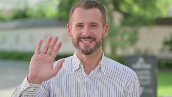 Outdoor Portrait of Middle Aged Man Waving at Camera Welcoming