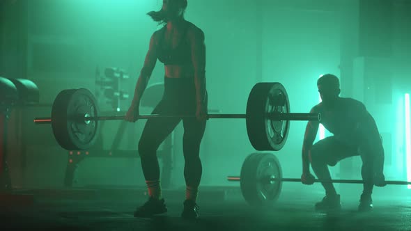 A Man and a Woman in a Colored Neon Red and Blue Light in Slow Motion Lift Heavy Barbells Over Their