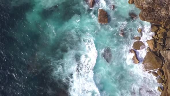 Top down aerial bird eye view of very strong and danger ocean waves crashing on to the rocks. Stunni