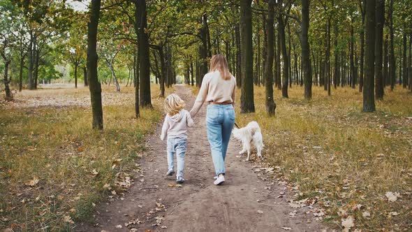 Young Mother and Little Daughter are Talking and Smiling Holding Hands Walking By Path in Autumn