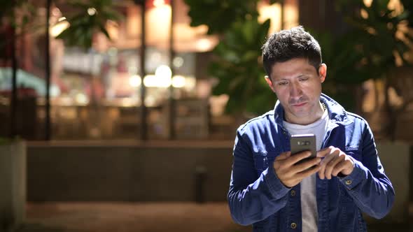 Hispanic Man Using Phone While Exploring the City Streets at Night