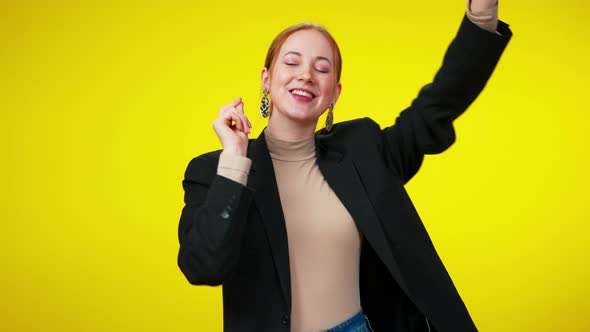 Cheerful Redhead Businesswoman with Toothy Smile Dancing at Yellow Background Looking at Camera