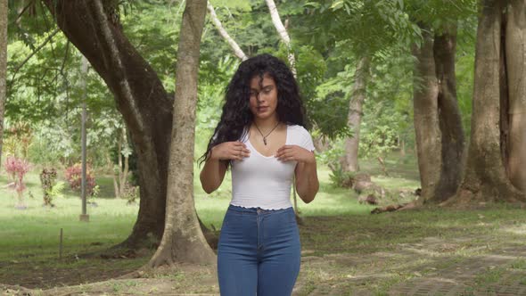 Young hispanic girl walks on a brick path at a park while playing in her hair