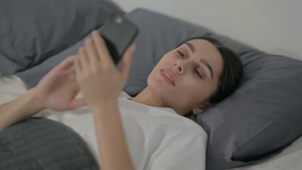 Close up of Hispanic Woman using Smartphone while Laying in Bed