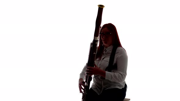 Silhouette Woman Plays Bassoon Music Sitting on Chair in Studio White Background Front View