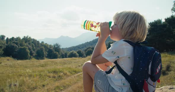 Child on Hike Journey Sit on Rock and Drink Water From Bottle on a Break