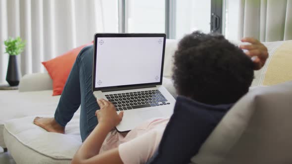 Happy african american woman sitting on sofa, using laptop with copy space