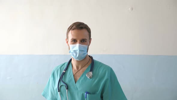 Portrait of Young Male Caucasian Doctor with Medical Face Mask Looks at Camera