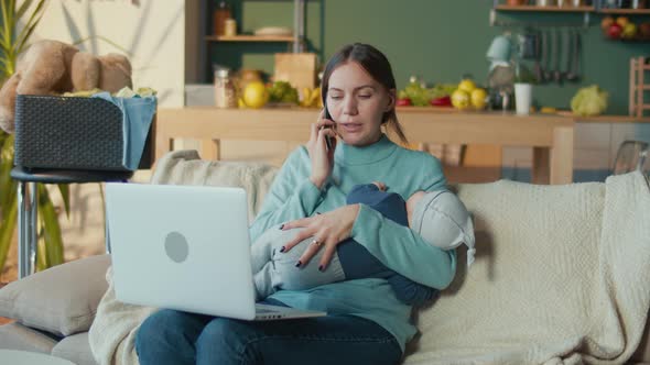 Business Mother Holding Infant and Answers the Call While Working