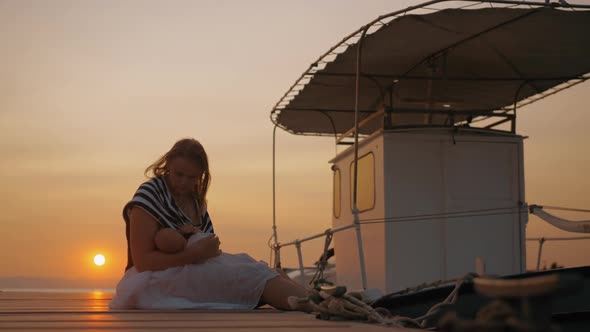 Mother Breastfeeding Baby in Quay at Sunset