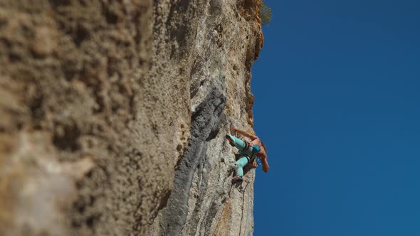 Bottom View of Muscular Strong Man Rock Climber Climbs on Vertical Cliff on Rock Wall on Blue Sky