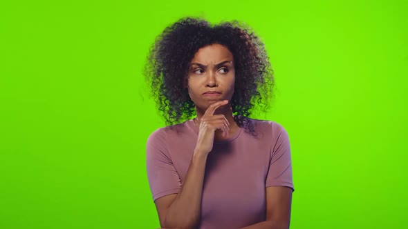 Young Indecisive African American Woman Stands on Green Background in Studio