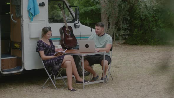 Man working at laptop and woman reading the book in summer camping.