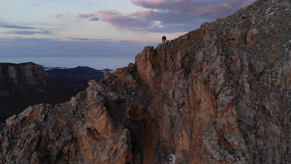 Aerial View of a Young Couple of Athletes Travelers Stands in the Mountains at Sunset in an Embrace