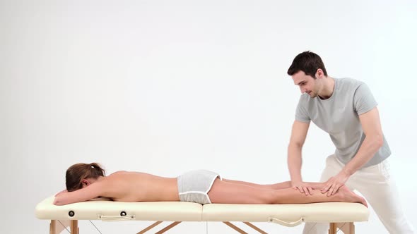 Male masseur with strong hands massaging lower part of leg to young woman lying on massage table