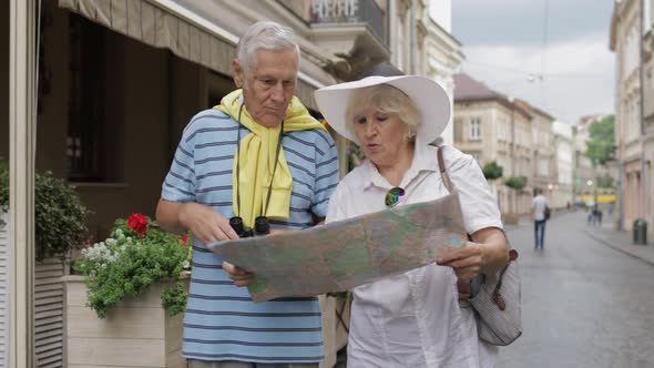 Senior Male and Female Tourists Walking with a Map in Hands Looking for Route