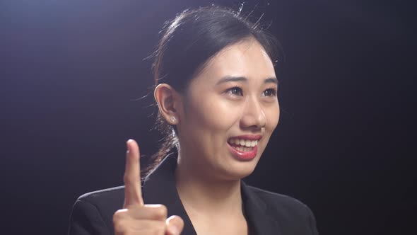 Side View Of Asian Speaker Woman Showing Index Fingers Up While Speaking In The Black Screen Studio