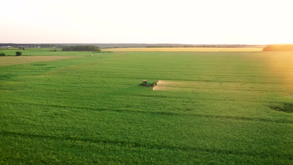 Tractor Trailer Sprays Fertilizers On Field Of Agricultural Crops Against Sunset