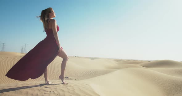 Fit Young Woman Wearing Red Dress is Posing on Top of a Dune Sunset