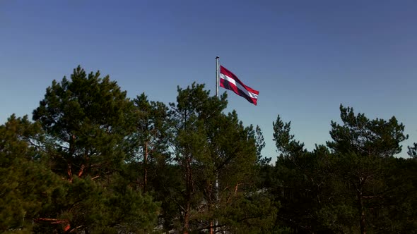 Establishing Revealing Shot of National Latvian Flag Behind Trees with Highway in Background