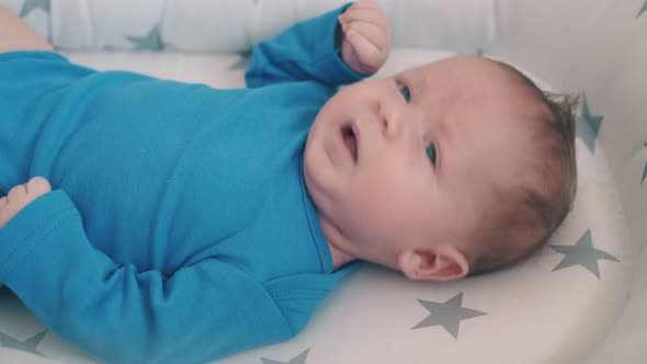 Small Child in Blue Bodysuit Kicks Bare Legs Lying in Cocoon