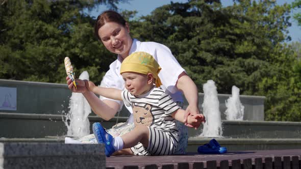 Mother with a Child Near Fountain of Public Park on a Hot Summer Day Funny Kid Eating Ice Cream