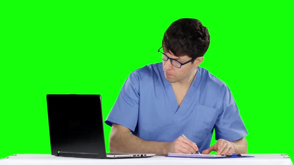 Male Doctor Writing at Desk in His Office Making Prescription. Green Screen