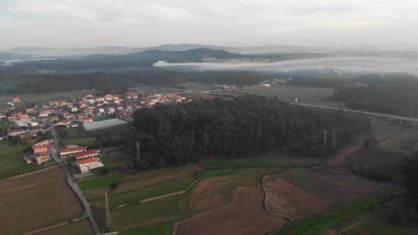 Aerial shot of village in the middle of trees and grass fields with fog.