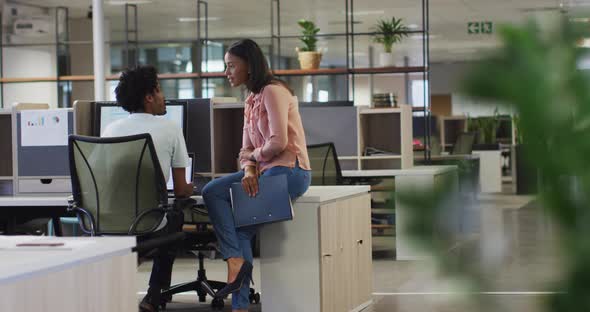 Video of diverse businesswoman and businessman using laptop and talking in office