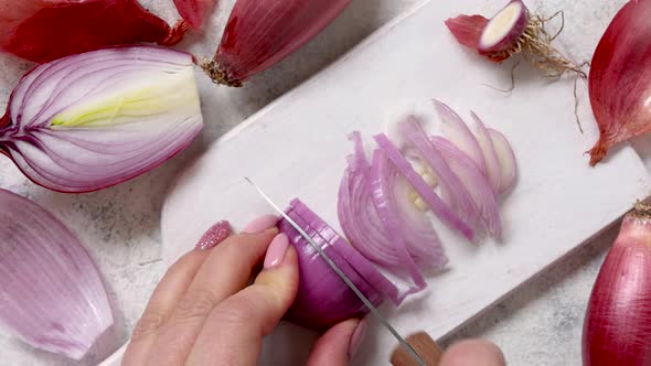 Woman's hands chopping fresh tropea red onion on a wooden board close up