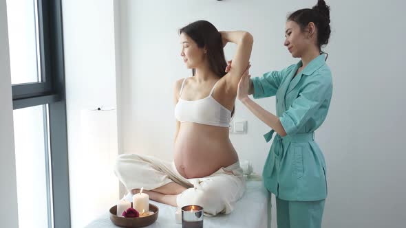 Masseur Physiotherapist in Blue Uniform Massaging Back of Pregnant Woman in Spa Center