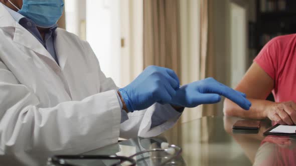 Male doctor visiting senior mixed race woman putting on gloves