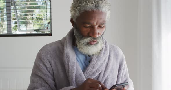 Senior man sneezing while using smartphone at home