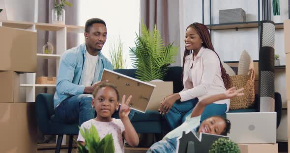 Black-Skinned Couple with Small Girls Moving Into New Own Apartment and Unpacking Carton Boxes