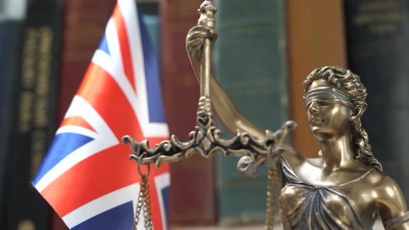 Statue of Lady Justice with Bookshelf with Books and UK Flag Background