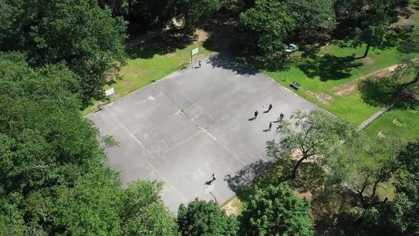 An aerial view over people playing basketball on a court is surrounded by beautiful green trees. The