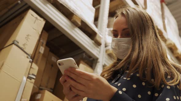 Female Worker Wearing a Protective Mask Uses a Smartphone to Check the Store's Stock